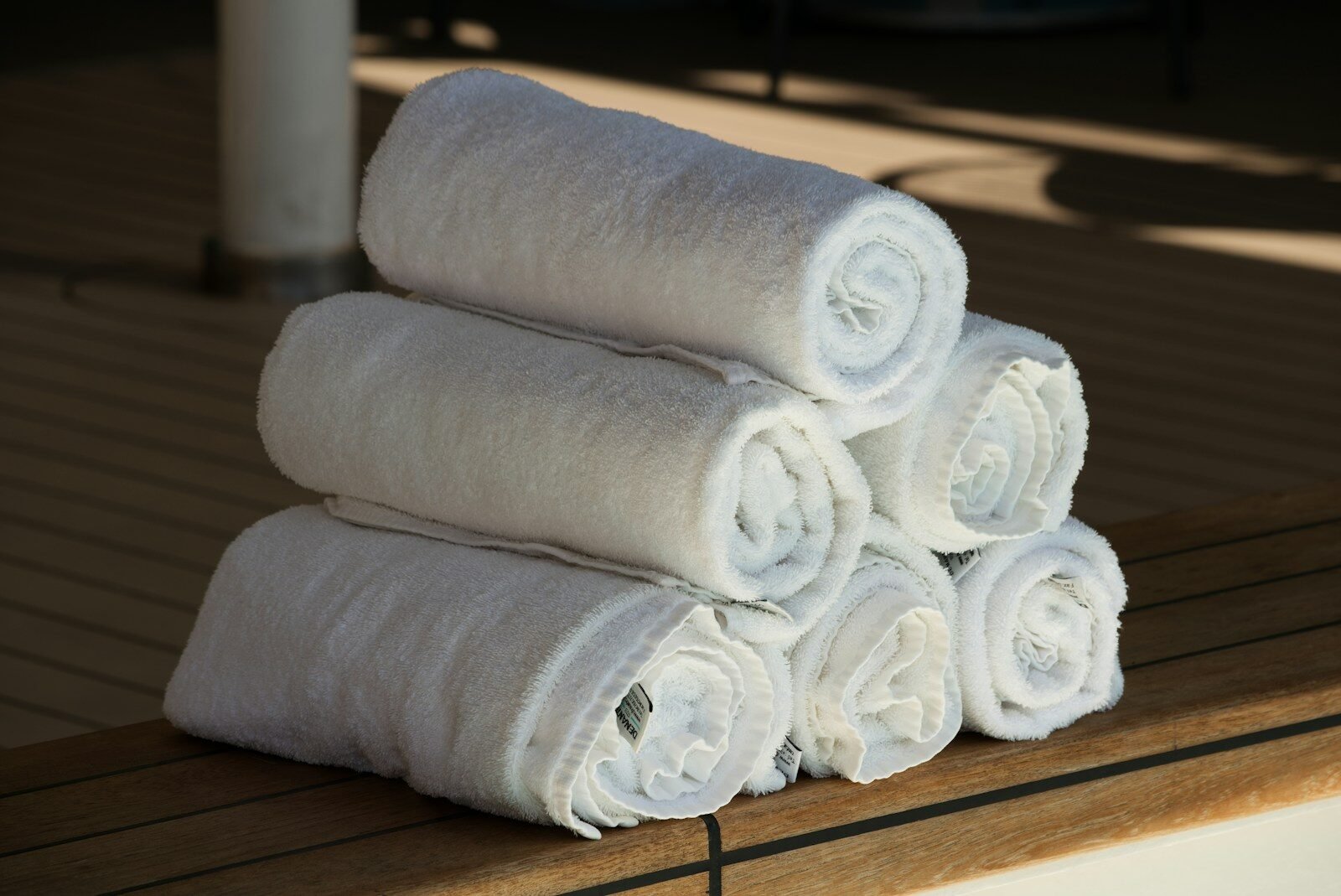 A stack of six white rolled towels on a wooden deck