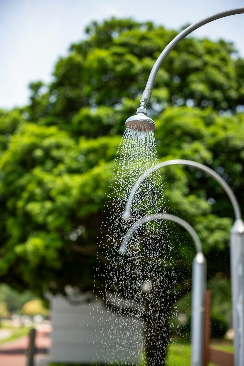 An outdoor shower spraying water with green trees in background