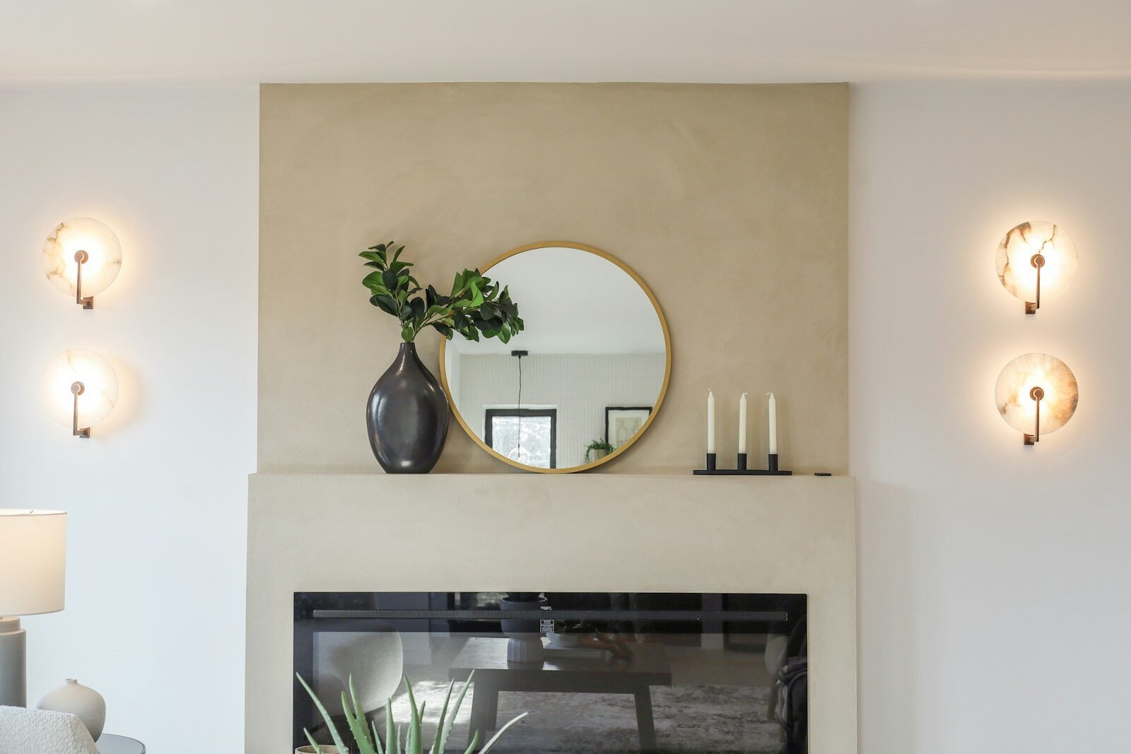 Modern fireplace with round mirror and decorative sconces