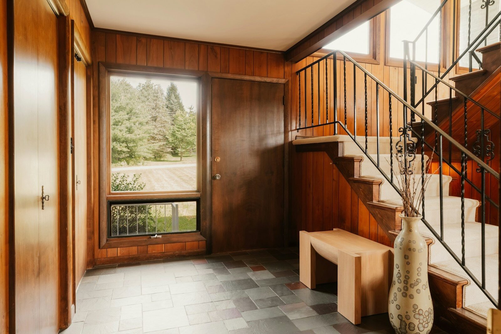 A wooden entryway with a staircase, slate floor, and a view of trees