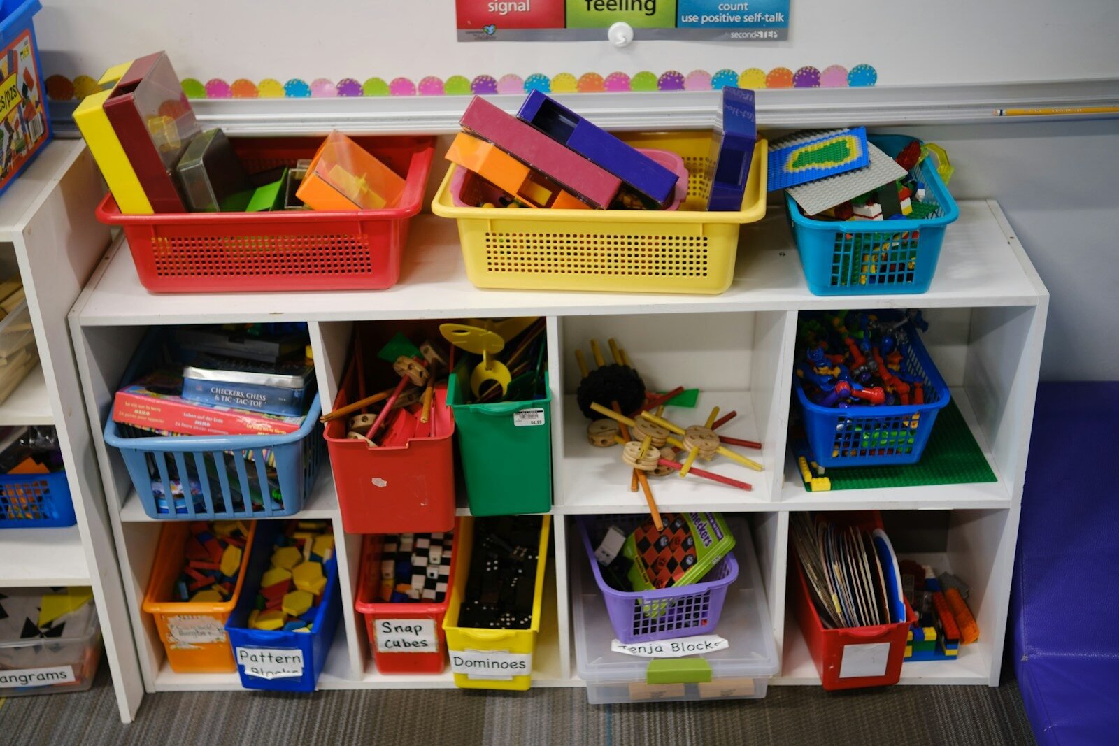 Colorful plastic storage bins filled with various educational toys on white classroom shelves