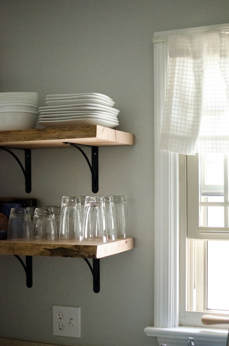 Kitchen shelves with white dishes, clear glasses, and a window